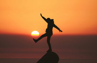 A person balancing on a rock with a sea and a sunset in the background