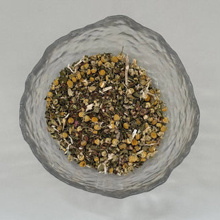 Glass bowl filled with dried herbs on a light grey background