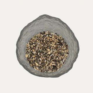 Glass container filled with a mix of dried herbs on a grey background