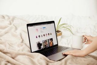 Person using a laptop on a bed with a plant and mug in the background